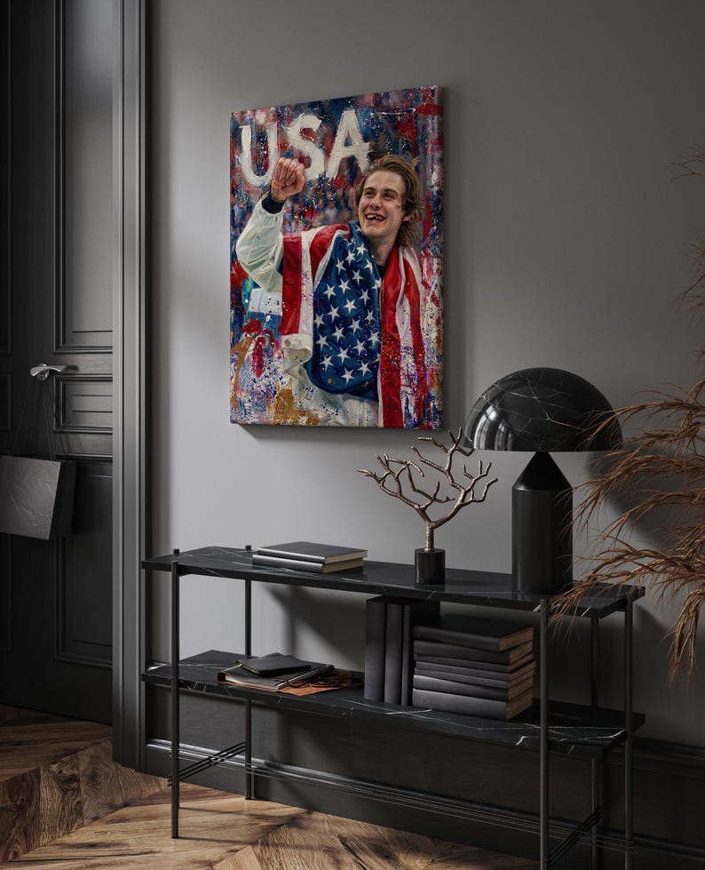 Pode incluir: Uma impress&atilde;o em tela emoldurada com uma pessoa envolta em uma bandeira americana, com a palavra "USA" vis&iacute;vel. A obra de arte &eacute; exibida acima de uma consola de m&aacute;rmore preto com objetos decorativos.