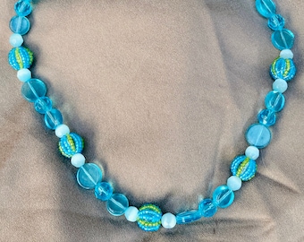 Puede incluir: Un collar de cuentas azules y verdes con un cierre plateado. Las cuentas son una mezcla de formas redondas y ovaladas.