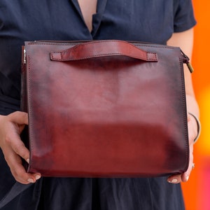 May include: A burgundy leather handbag with a top handle and a zip closure.