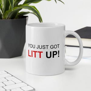 Op de afbeelding: Witte keramische koffiemok met zwarte tekst die "You just got LITT UP!" luidt. Het woord "LITT" is rood.