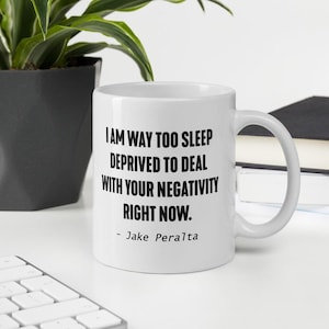 May include: White ceramic coffee mug with black text that reads "I am way too sleep deprived to deal with your negativity right now. - Jake Peralta"