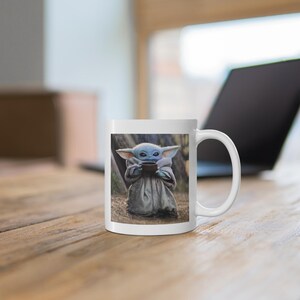 Puede incluir: Taza de cer&aacute;mica blanca con una imagen colorida de un personaje ficticio sosteniendo una taza. El personaje es azul, verde y marr&oacute;n con orejas grandes. La taza tiene un asa en el lado derecho.