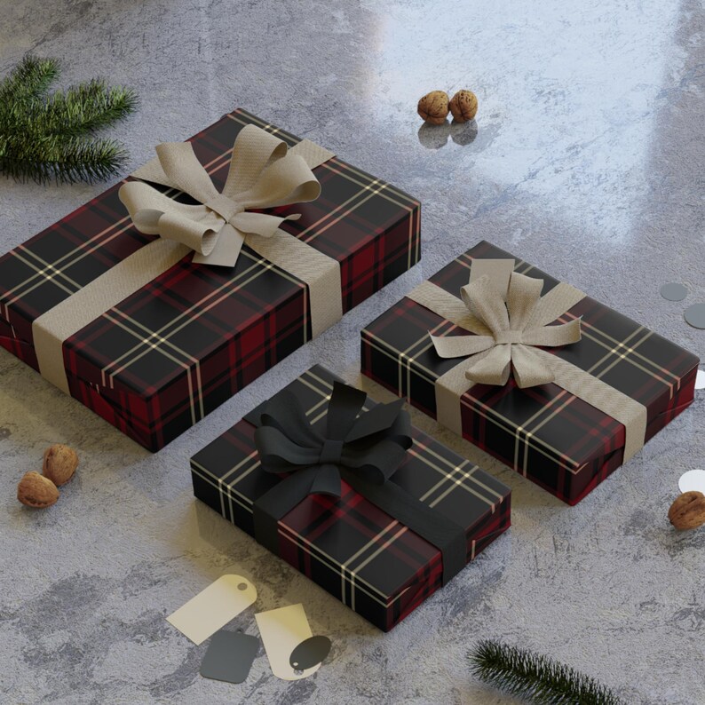 K&ouml;nnte beinhalten: Drei verpackte Geschenke mit kariertem Papier in Schwarz, Rot und Gold. Jedes Geschenk ist mit einem Band und einer Schleife gebunden. Die Schleifen sind beige und schwarz. Die Geschenke liegen auf einer grauen Oberfl&auml;che mit dekorativen Elementen.