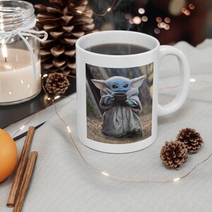Puede incluir: Taza de cer&aacute;mica blanca con una imagen colorida de un personaje ficticio sosteniendo una taza. El personaje es verde, azul y marr&oacute;n con orejas grandes. La taza est&aacute; sobre una superficie gris claro.