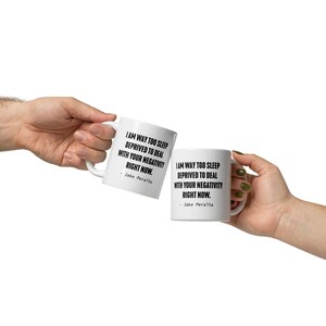 May include: Two white coffee mugs with black text. The text on the mugs reads "I am way too sleep deprived to deal with your negativity right now. - Jake Peralta".