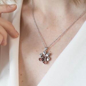 May include: A silver necklace with a paw print pendant. The pendant has a small, round, red gemstone in the middle. The necklace is on a delicate chain. The background is white.