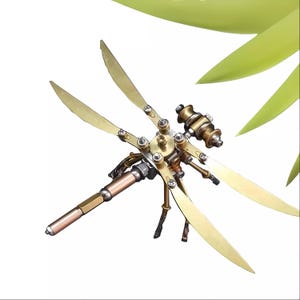 以下が含まれることがあります： 複雑なディテールとギアを備えた金色の金属製のトンボの彫刻。トンボは4枚の羽と長く細い体を持っています。