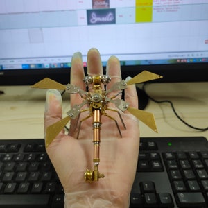 May include: A gold and silver metal dragonfly sculpture with intricate details. The dragonfly is posed with its wings spread out and its legs extended.