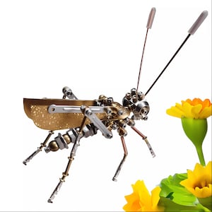 May include: A gold and silver metal grasshopper sculpture with a glittery finish. The grasshopper is posed with its legs extended and its antennae pointing upwards. The sculpture is set against a white background with a yellow flower in the background.