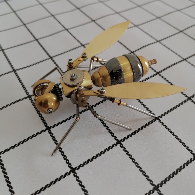 May include: A detailed steampunk-style metal wasp sculpture with gold and black accents. The wasp has intricate gears and moving parts, and its wings are spread wide.