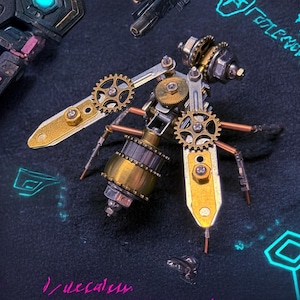 Peut inclure: Une sculpture mécanique détaillée de type steampunk représentant un insecte. L'insecte présente des engrenages, des plaques et des tiges de couleur laiton, or et argent. Le corps a une forme cylindrique avec des détails complexes. Les ailes sont faites de plaques dorées. Le fond est sombre avec des accents bleu néon.