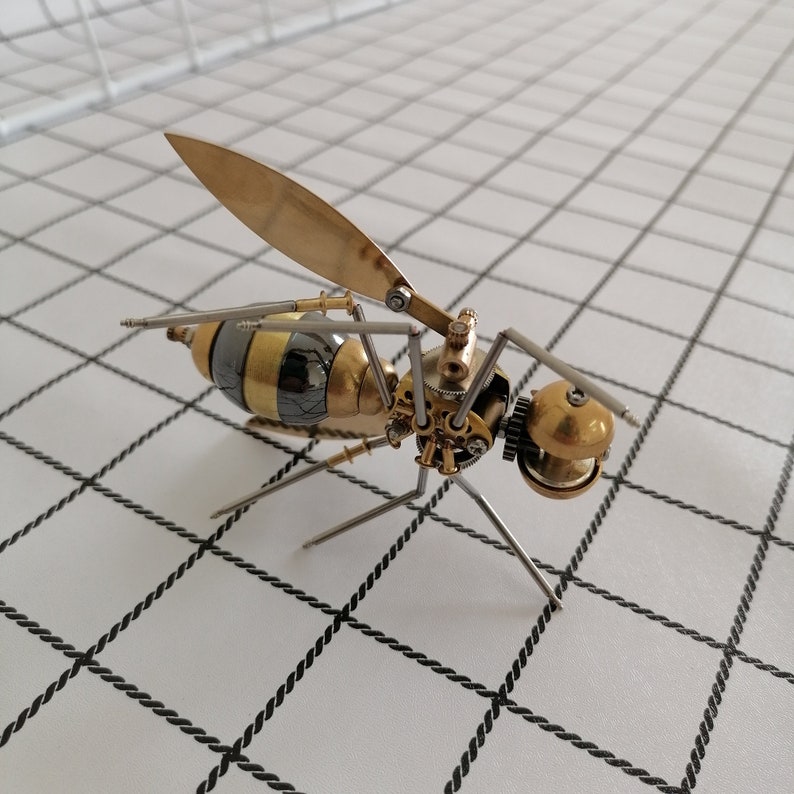 May include: A detailed steampunk-style metal wasp sculpture with gold and silver accents. The wasp has a large wingspan and intricate gears and mechanisms.