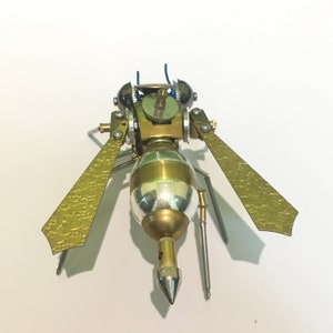 May include: A gold and silver steampunk-style wasp sculpture with intricate details and gears. The wings are made of metal and have a textured surface.
