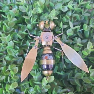 May include: A steampunk-style metal wasp sculpture with gold wings and a black and gold striped body. The sculpture is made of gears, metal, and other intricate details.
