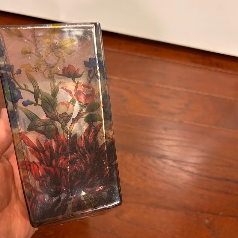 Pu&ograve; includere: Un vaso rettangolare in vetro con un motivo floreale. Il vaso presenta una variet&agrave; di fiori nelle tonalit&agrave; del rosso, rosa, giallo e blu. I fiori sono su uno sfondo chiaro. Il vaso &egrave; tenuto in mano da una persona.