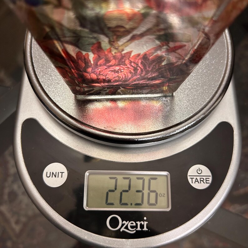 Pu&ograve; includere: Una ciotola decorativa in vetro con un motivo floreale, appoggiata su una bilancia da cucina digitale. La bilancia mostra un peso di 634.05 grammi. La bilancia &egrave; argentata e nera, con il marchio "Ozeri" visibile.