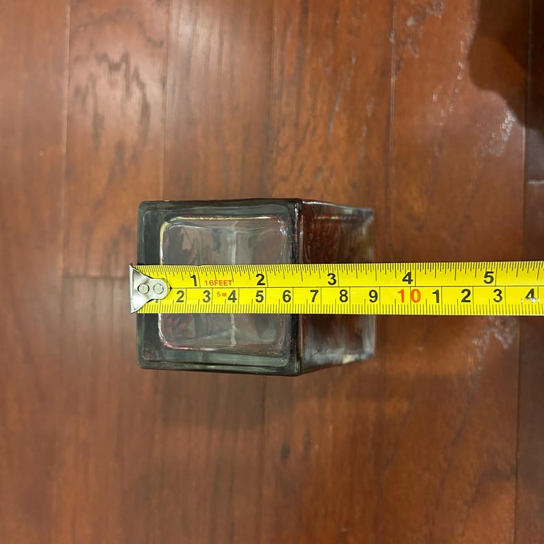 Pu&ograve; includere: Un vaso di vetro trasparente e rettangolare con una tinta scura. Il vaso &egrave; largo circa 7,6 cm. Un metro a nastro giallo &egrave; posto sopra il vaso, mostrando la misura in centimetri.