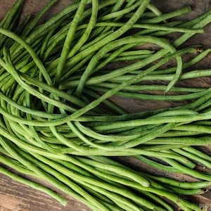 May include: A bunch of long, green string beans on a wooden surface.