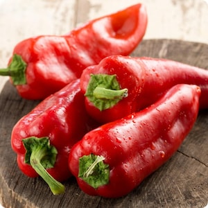 May include: A collection of bright red peppers, each with a green stem and leaf, are displayed. The peppers have a smooth, glossy skin and are slightly wet, with water droplets visible. They are presented on a weathered wooden surface, highlighting their fresh, natural quality.