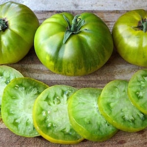 May include: Green tomatoes sliced on a wooden chopping board. The tomatoes are a pale green colour with yellow streaks. The slices are arranged in a semi-circle.