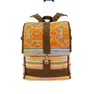 Könnte beinhalten: Ein brauner Canvas-Rucksack mit bunten Stickereien. Der Rucksack hat eine Klappe mit einem braunen Lederriemen und einer Metallschnalle.
