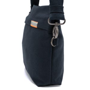 May include: A dark blue canvas crossbody bag with a silver clasp and a black strap. The bag has a small label with the word "SEBAGUO" on it.