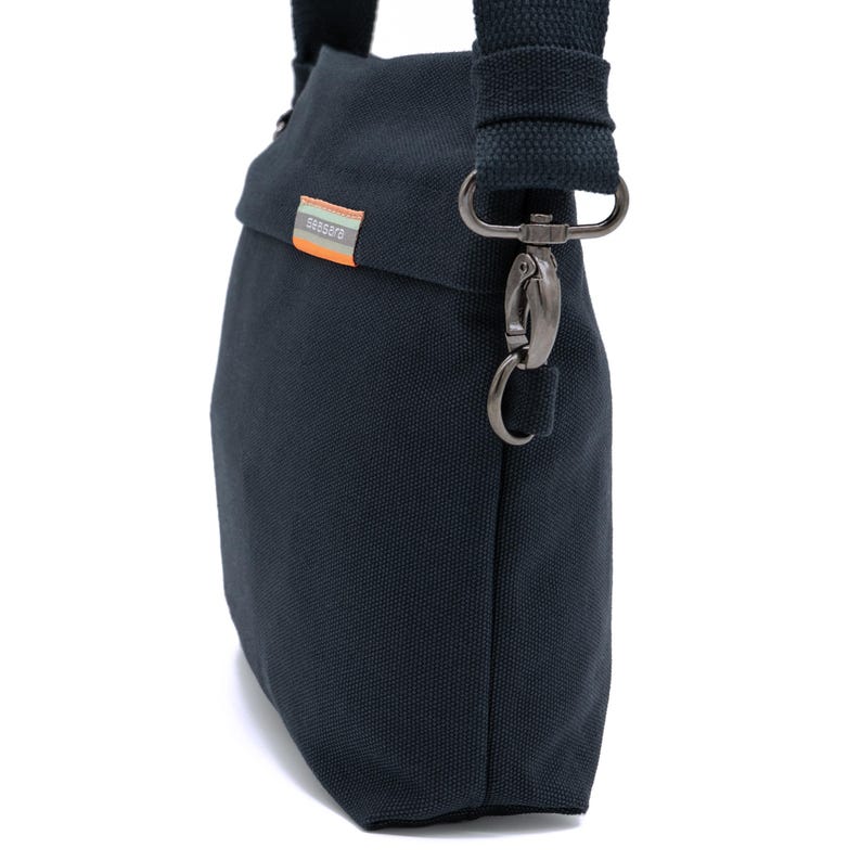 May include: A dark blue canvas crossbody bag with a silver clasp and a black strap. The bag has a small label with the word "SEBAGUO" on it.