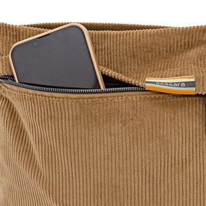 Op de afbeelding: Close-up van een bruin corduroy tas met een zwarte rits en een smartphone in de zak. De tas heeft een label met het woord "seasara" in witte tekst op een gestreepte achtergrond van oranje, blauw en groen.