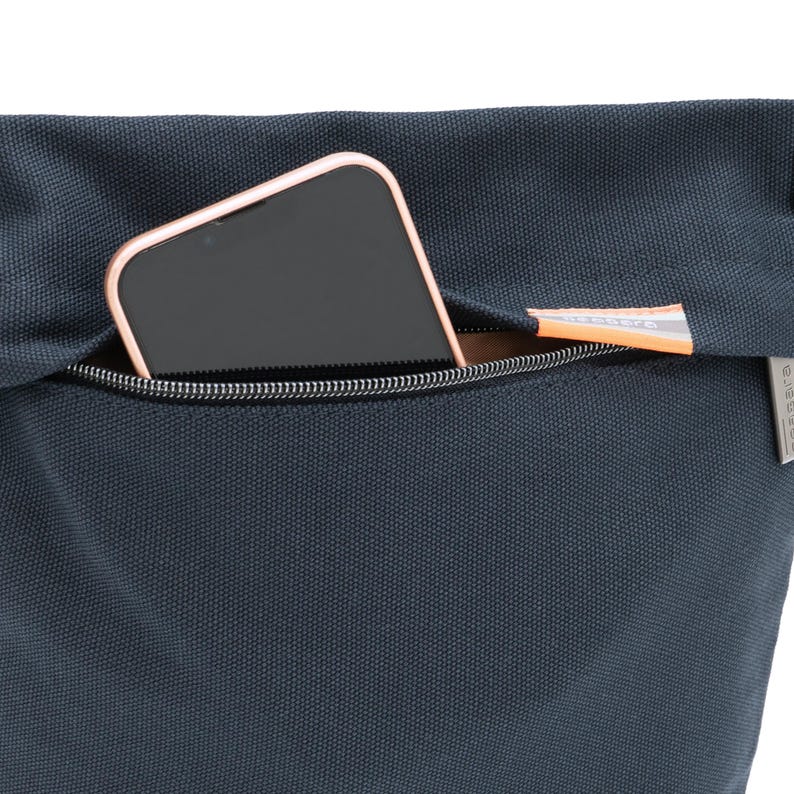May include: A dark blue canvas bag with a zipped pocket. A smartphone is inside the pocket.