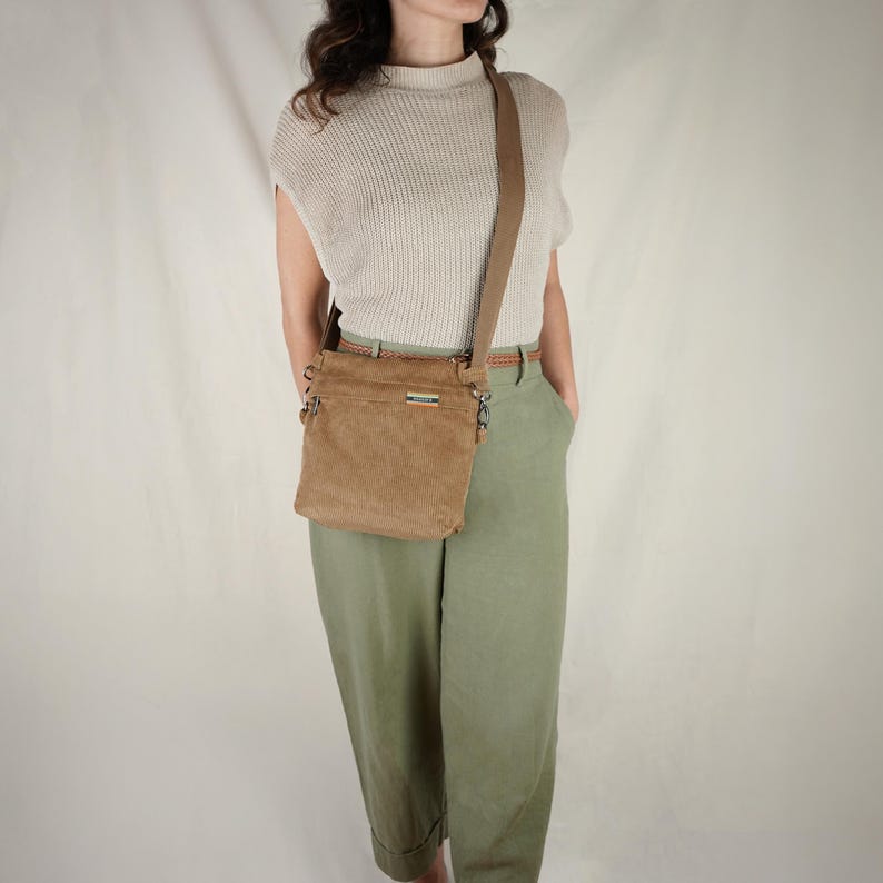 Op de afbeelding: Een bruin corduroy crossbody tas met een bijpassende verstelbare riem. De tas heeft een rechthoekige vorm met een voorvak en zilverkleurige hardware. De tas wordt over de schouder gedragen.