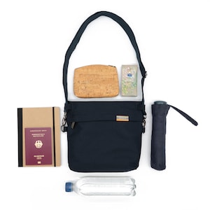 May include: A black crossbody bag with a cork wallet, a small package, a passport, a notebook, a water bottle and a black umbrella.