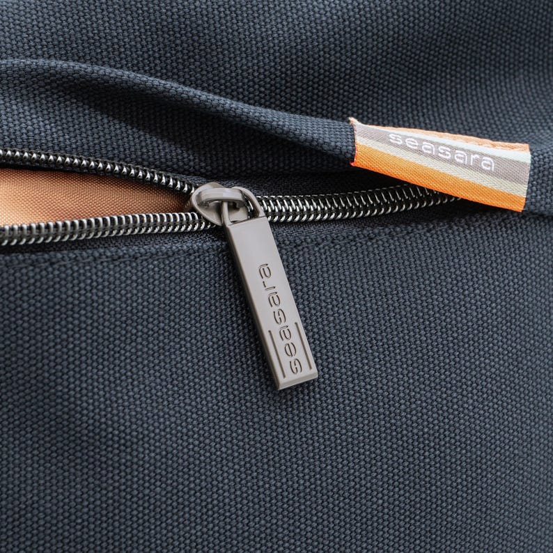 May include: Close-up of a black zipper with a silver zipper pull. The zipper pull has the word "seasara" printed on it.