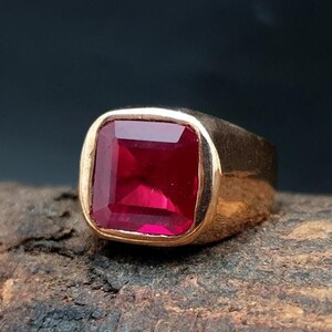 Op de afbeelding: Een gouden ring met een vierkante, dieprode edelsteen.