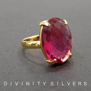 May include: A gold ring with a large, oval-shaped, faceted, pink gemstone.