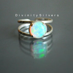 May include: A silver ring with a round opal gemstone. The opal has a light blue, green, and orange iridescent sheen.