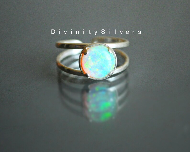 May include: A silver ring with a round opal gemstone. The opal has a light blue, green, and orange iridescent sheen.