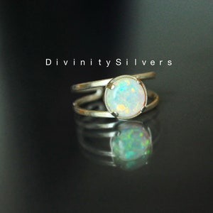 May include: A silver ring with a white opal gemstone. The ring has a double band design. The text "Divinity Silvers" is visible in the background.