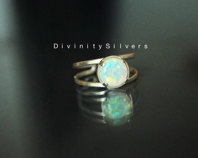 May include: A silver ring with a white opal gemstone. The ring has a double band design. The text "Divinity Silvers" is visible in the background.