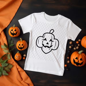 Könnte beinhalten: Weißes T-Shirt mit einer schwarzen Umrandung eines Jack-o'-Lantern-Kürbisses mit einem lächelnden Gesicht. Das Shirt ist von kleinen orangefarbenen Kürbissen umgeben.