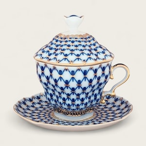 May include: A blue and gold porcelain teacup and saucer set with a lid. The cup and saucer feature a geometric pattern with gold accents.