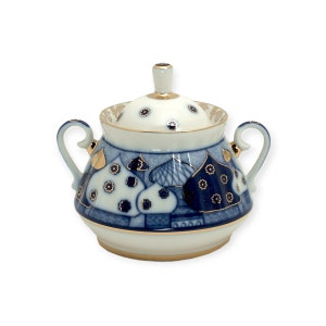 Peut inclure: Sucrier en porcelaine blanc et bleu, orné d'un motif de bâtiments et de fleurs. Le sucrier est doté d'un couvercle, de deux anses et de détails dorés. Un objet décoratif pour servir le sucre.