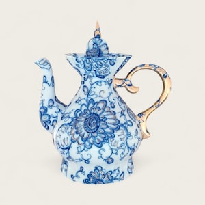Peut inclure: Une théière en porcelaine bleue et blanche avec une poignée et un couvercle dorés. La théière est décorée d'un motif floral.