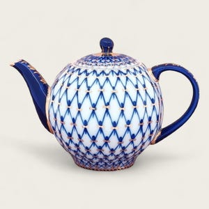 Puede incluir: Una tetera de porcelana azul y blanca con ribete dorado y un patrón geométrico. La tetera tiene un cuerpo redondo y un pico en el lateral.