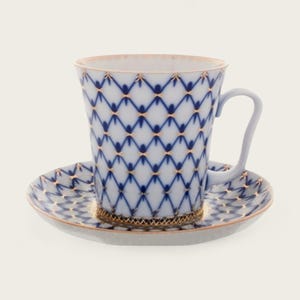 May include: A white porcelain teacup and saucer set with a blue and gold geometric pattern. The cup has a flared shape and a handle. The saucer has a matching pattern.
