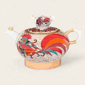 May include: White porcelain teapot with a gold trim and a rooster design. The rooster is painted in red, orange, yellow, green, and blue colors.