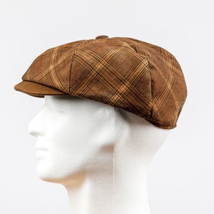 Puede incluir: Una gorra de estilo newsboy de cuadros marrones y beige con una visera marrón.
