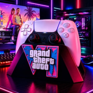 Könnte beinhalten: Ein weißer kabelloser Gamecontroller steht auf einem schwarzen Ständer mit einem rosa-blauen Grand Theft Auto VI-Logo. Der Ständer zeigt den Schriftzug Grand Theft Auto VI in weißen Buchstaben vor einem grafischen Palmenhintergrund.