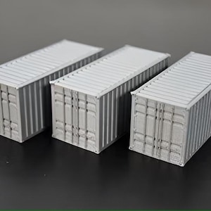 May include: Three gray metal shipping containers, each with a slightly different design, are arranged in a row on a gray surface.
