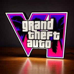 Puede incluir: Un letrero LED rectangular que presenta el logotipo de Grand Theft Auto en letras blancas. El fondo muestra un degradado vibrante de púrpura y rosa con siluetas negras de palmeras. El letrero está iluminado con un brillo intenso.