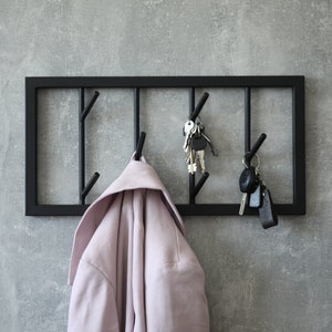 Puede incluir: Un perchero de metal negro con cinco ganchos, una chaqueta rosa colgada en un gancho y llaves colgadas en otros dos ganchos.